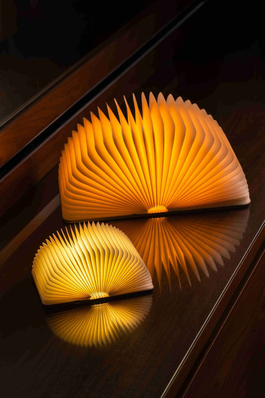 Two wooden book-shaped lamps on a reflective surface with a dark background