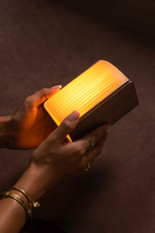 Hand holding a glowing wooden book against a dark background